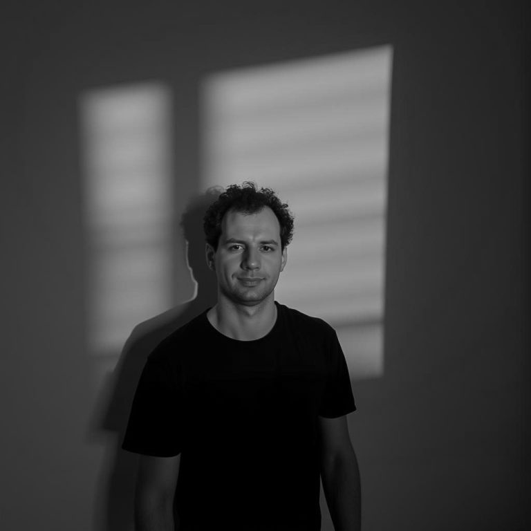 Mann in schwarzem T-Shirt, Schatten von Fenstergitter auf der Wand.