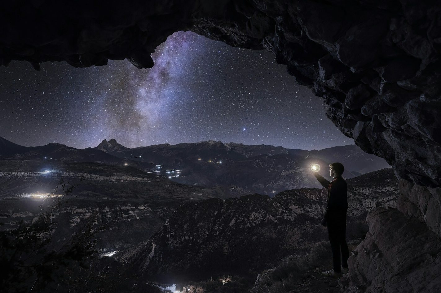 Mann steht in einer Höhle und zeigt mit einer Taschenlampe auf den Sternenhimmel.